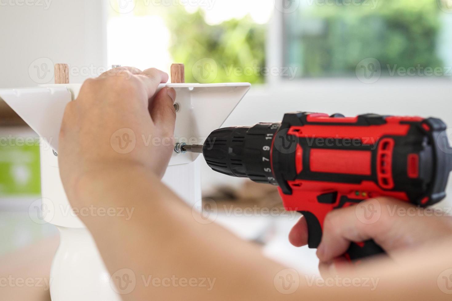 man assembling white table furniture at home using cordless screwdriver photo