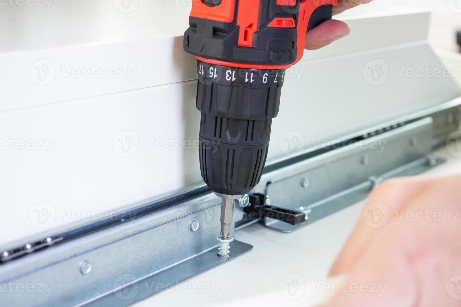 man assembling white table furniture at home using cordless screwdriver photo