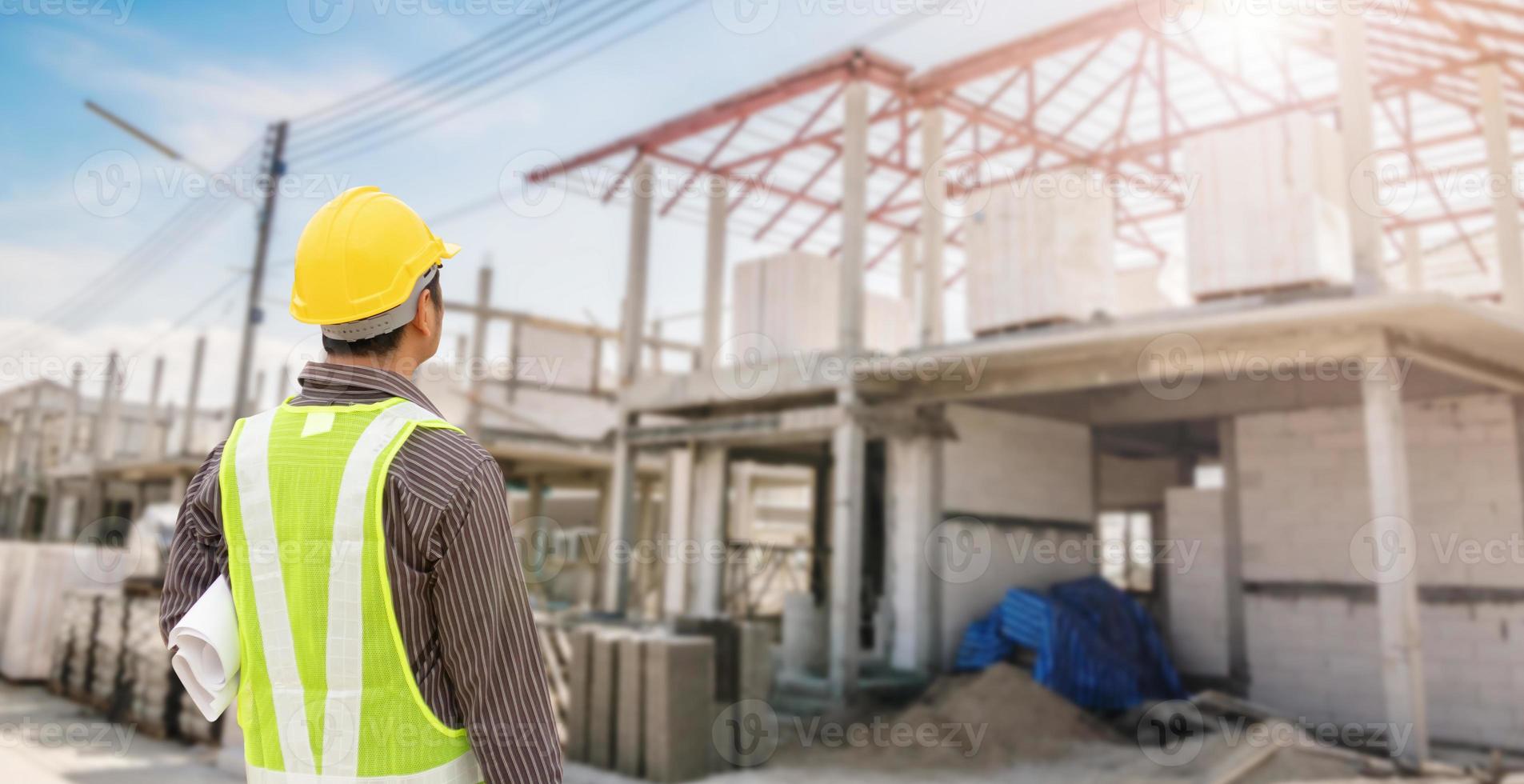 young professional engineer in protective helmet and blueprints paper at the house building construction site photo