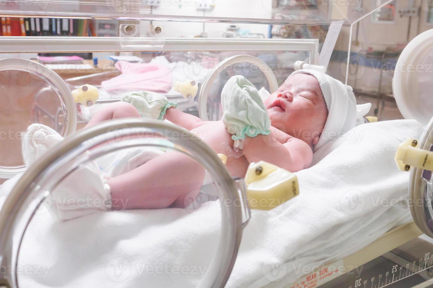 Newborn baby girl inside incubator in hospital post delivery room photo