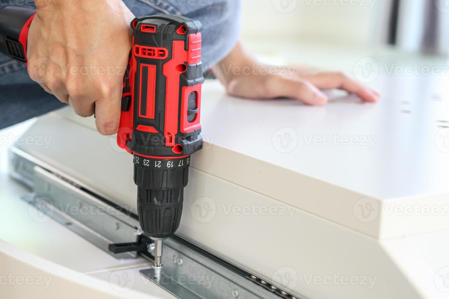 man assembling white table furniture at home using cordless screwdriver photo