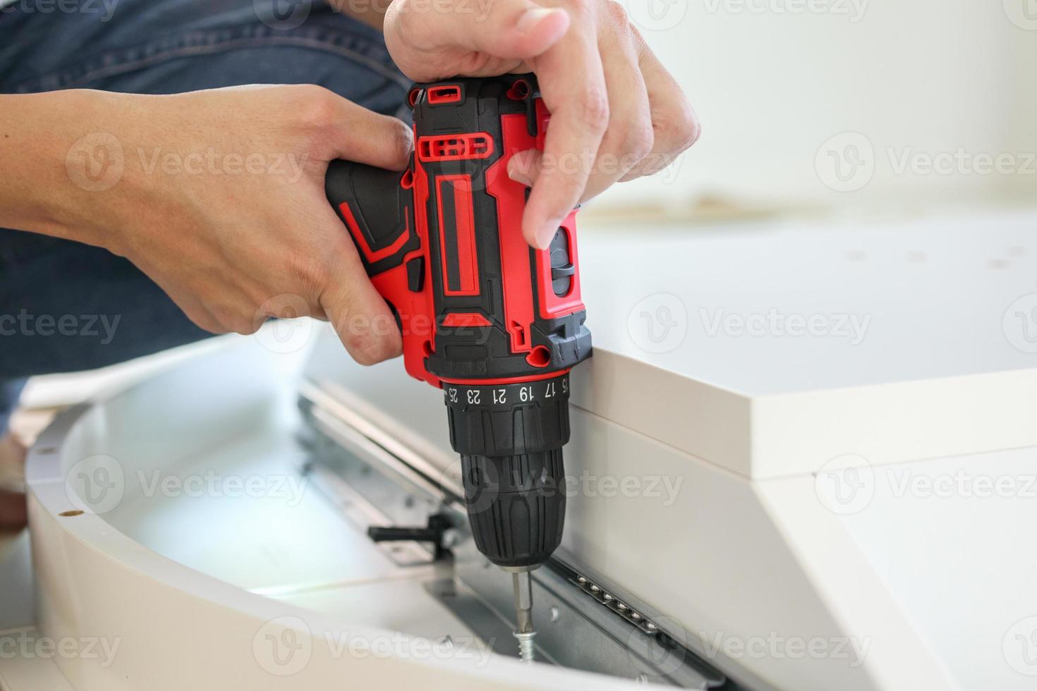 man assembling white table furniture at home using cordless screwdriver photo