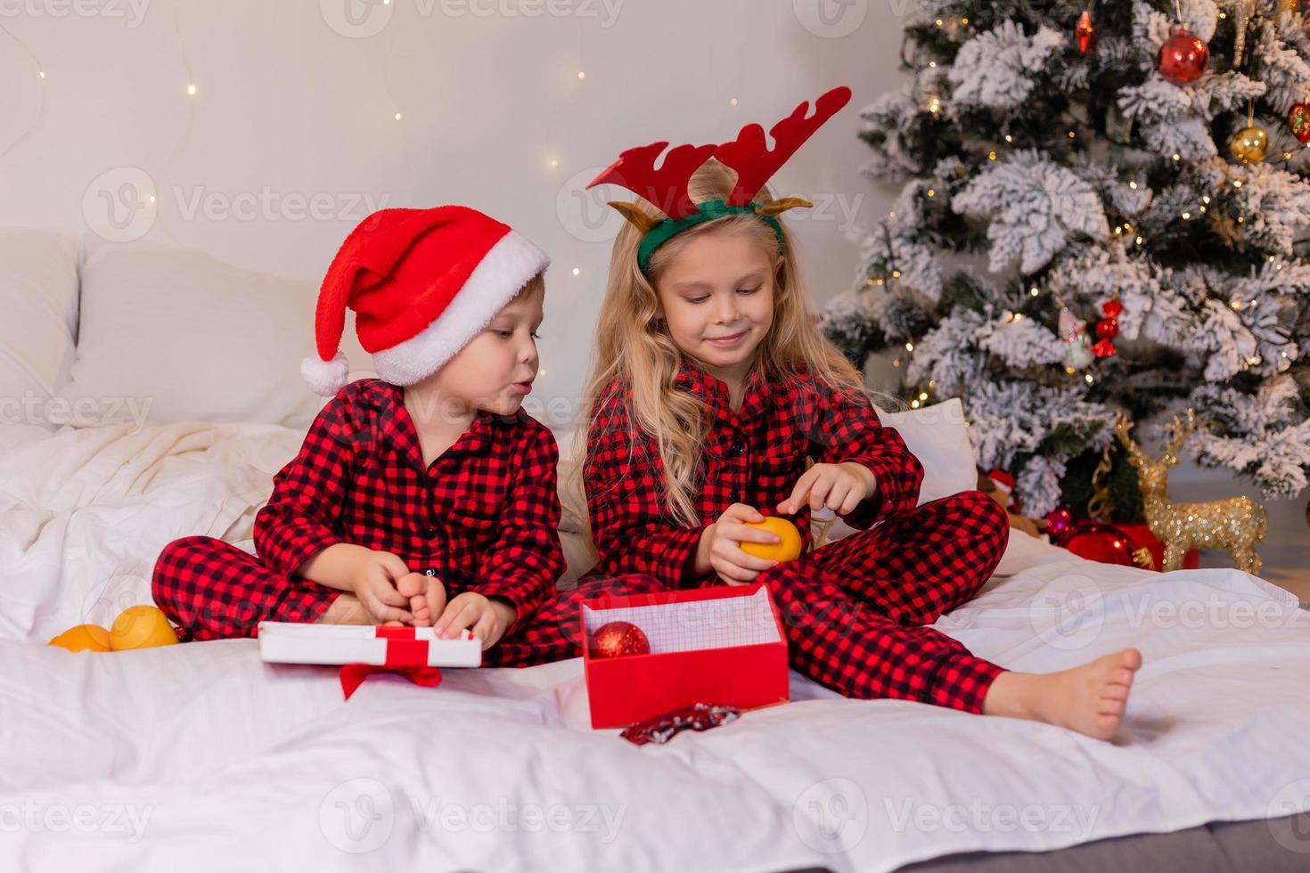 two happy children in pajamas for Christmas are sorting presents and playing with Christmas toys. High quality photo
