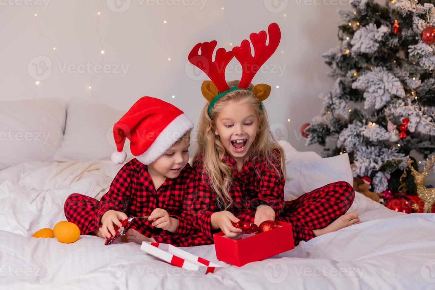 dos niños felices en pijama para navidad están clasificando regalos y jugando con juguetes navideños. foto de alta calidad