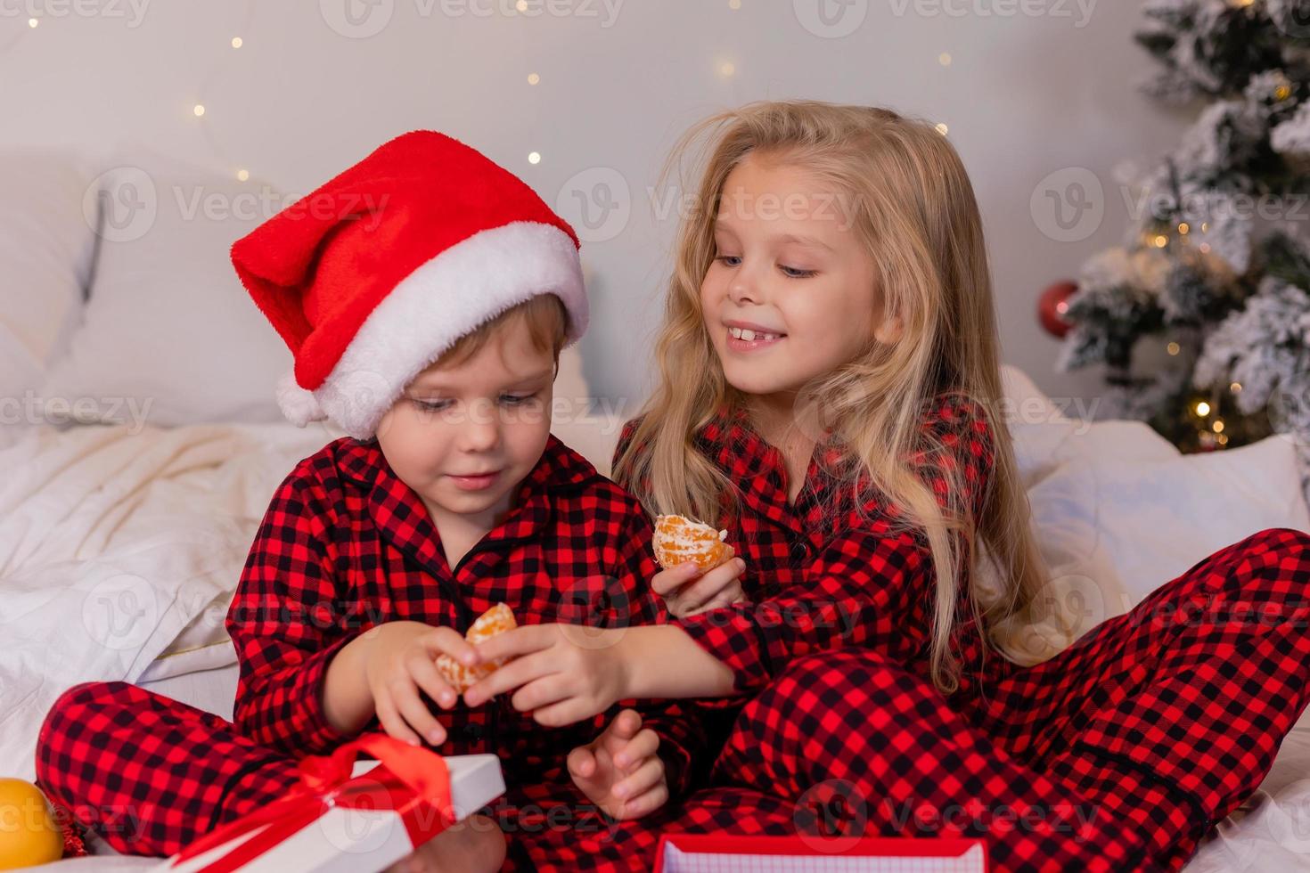 two happy children in pajamas for Christmas are sorting presents and playing with Christmas toys. High quality photo