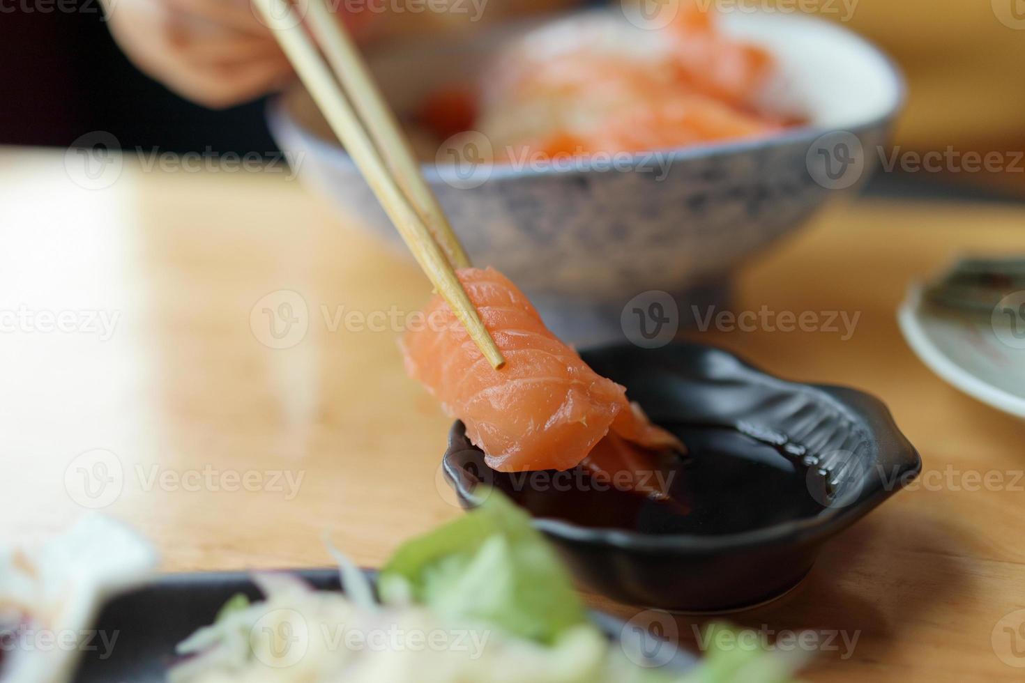 Salmon sashimi in chopsticks dipping with soy sauce photo