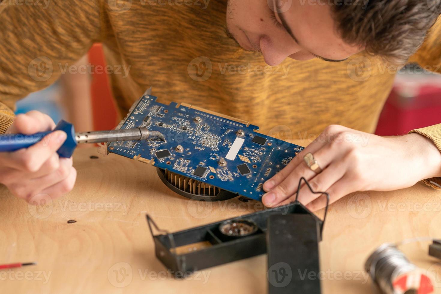 a young man solders a burnt-out microcircuit with a soldering iron photo