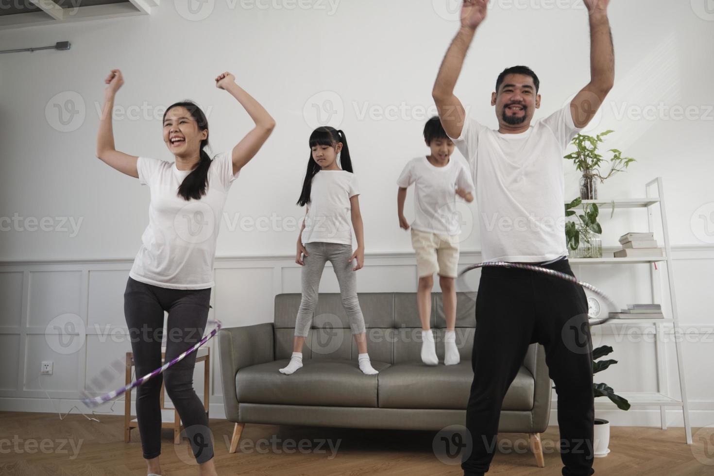 feliz bienestar familia tailandesa asiática, padres e hijos son divertidos jugando hula hoops juntos, entrenamiento físico y ejercicio saludable en la sala de estar blanca, el estilo de vida doméstico y la actividad de fin de semana. foto