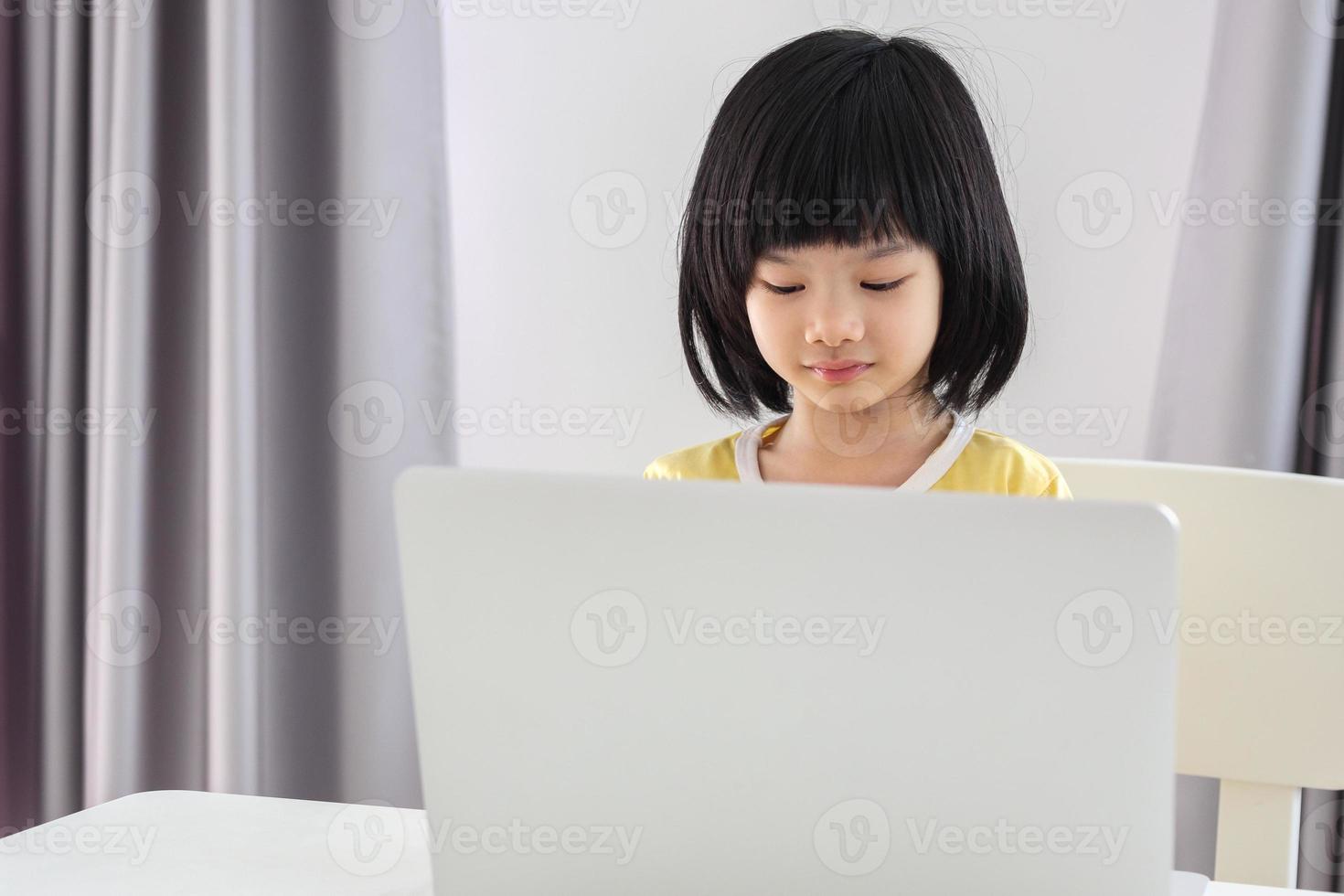 little asian girl student study online using laptop computer at home photo