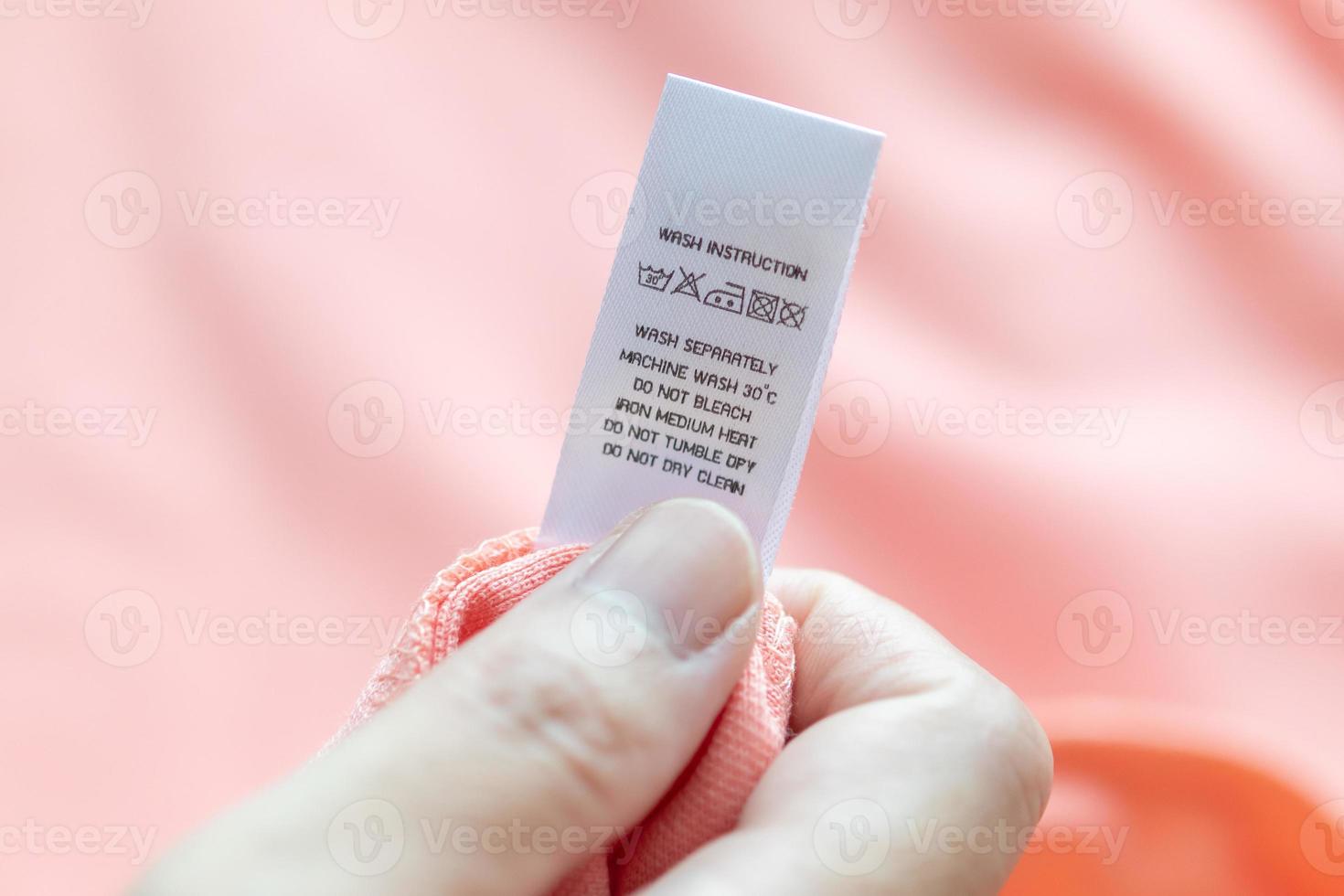 Hand hold and reading at white laundry care washing instructions clothes label on pink shirt photo