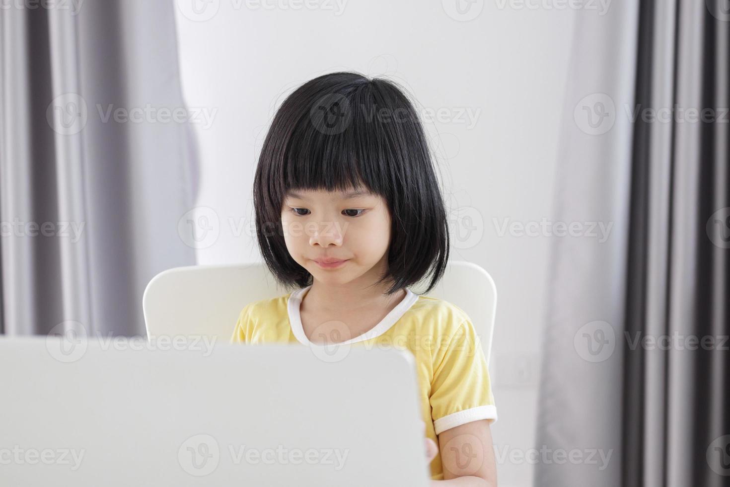 little asian girl student study online using laptop computer at home photo