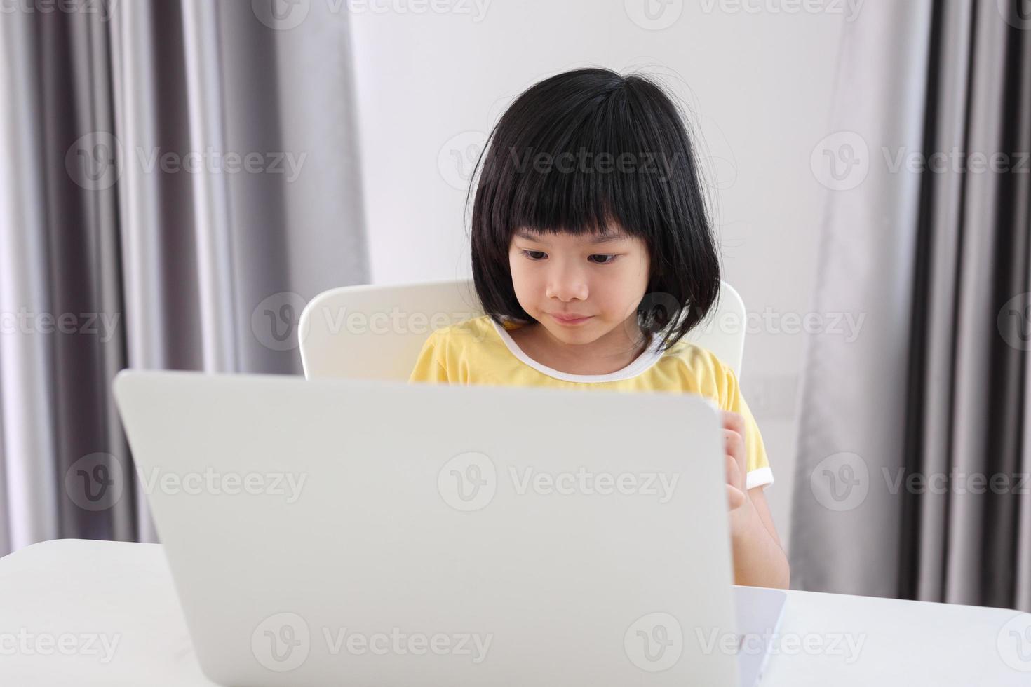 little asian girl student study online using laptop computer at home photo