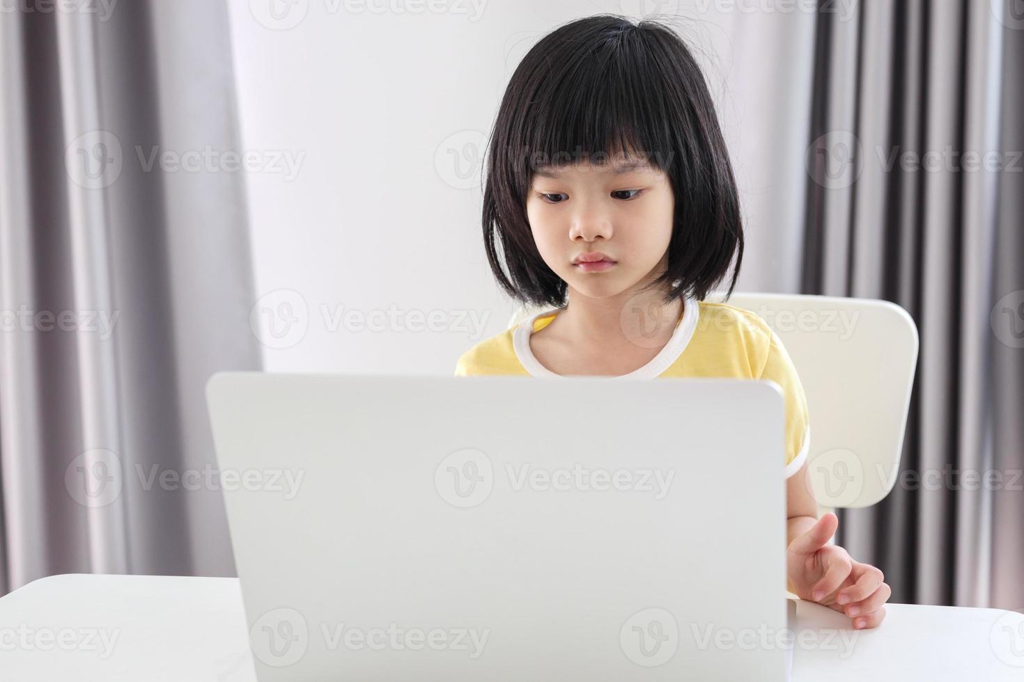 little asian girl student study online using laptop computer at home photo
