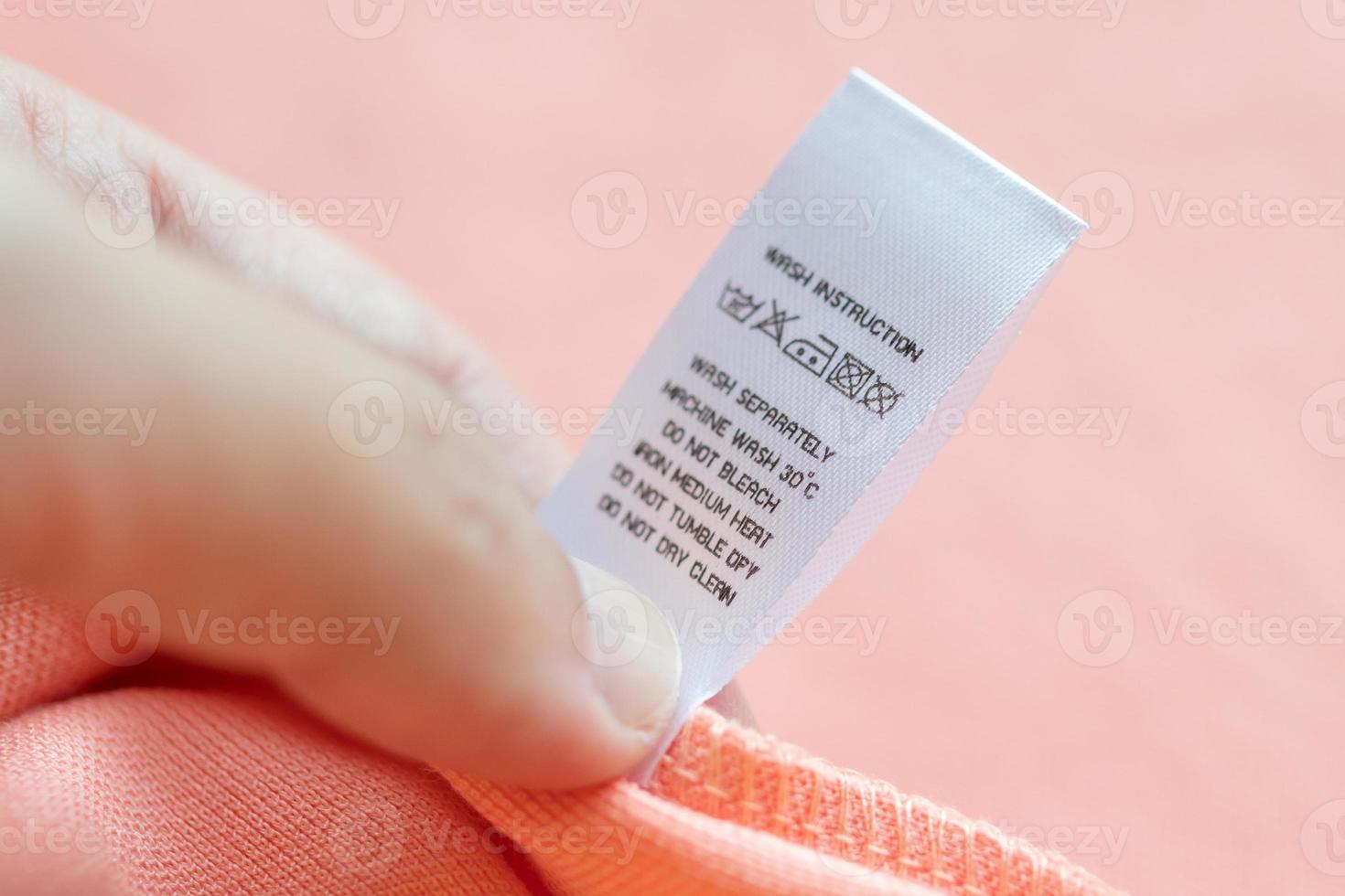 Hand hold and reading at white laundry care washing instructions clothes label on pink shirt photo