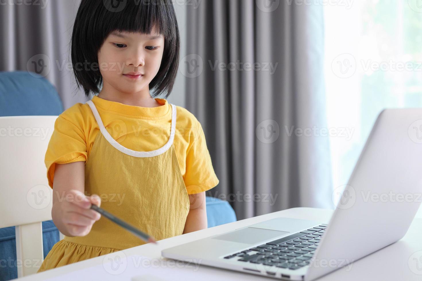 little asian girl student study online using laptop computer at home photo