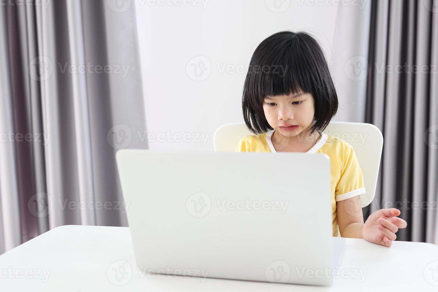 little asian girl student study online using laptop computer at home photo