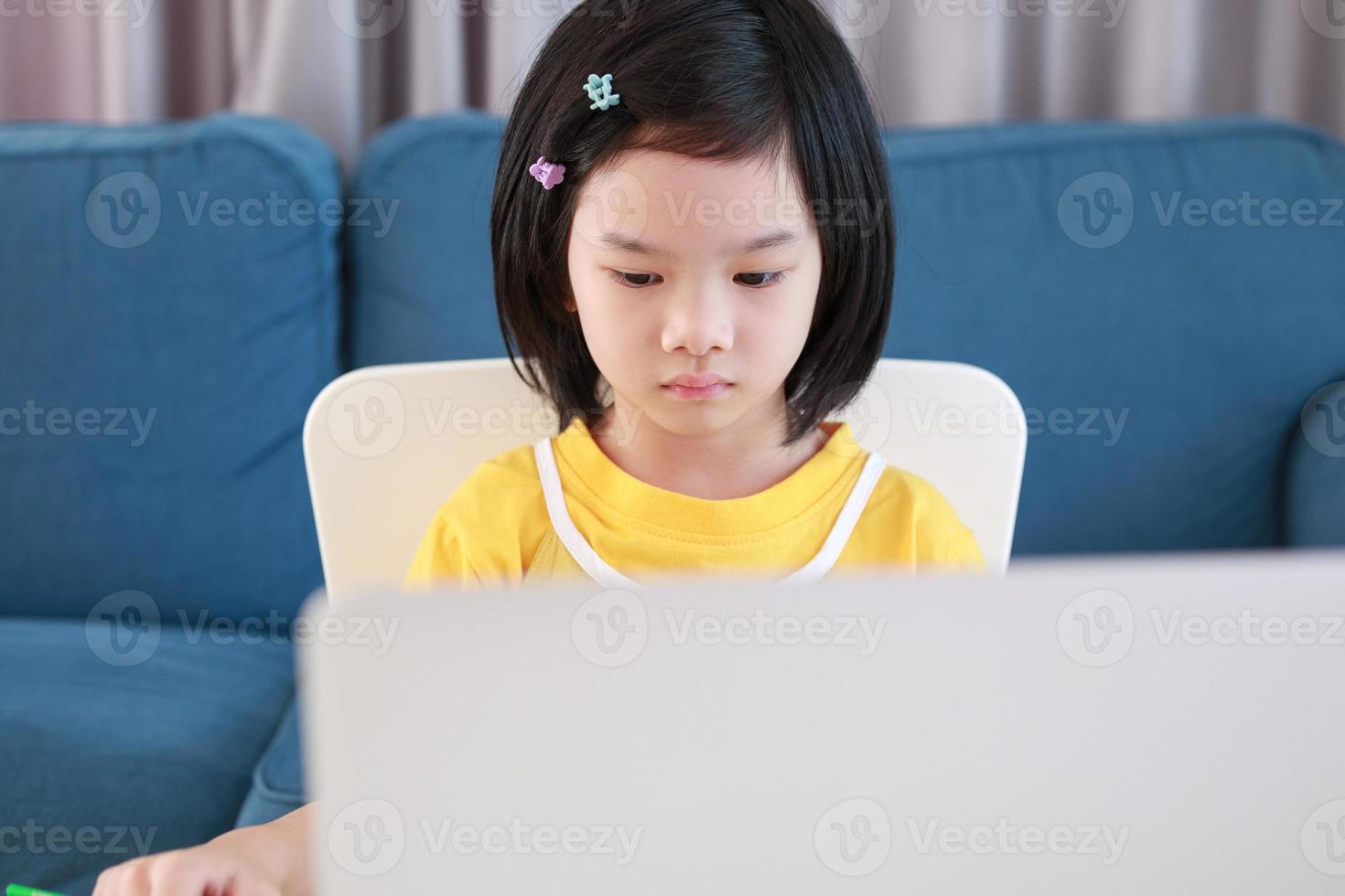 una pequeña estudiante asiática estudia en línea usando una computadora portátil en casa foto