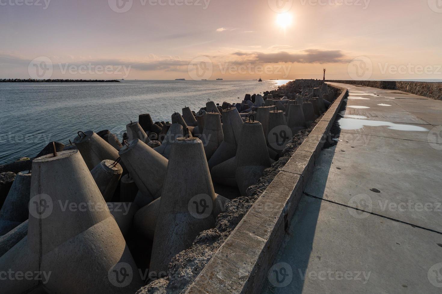 North pier with breakwaters, sunset seascape. Tetrapods along edges of pier. Beautiful evening seascape. Modern lighthouse in sunlight. photo