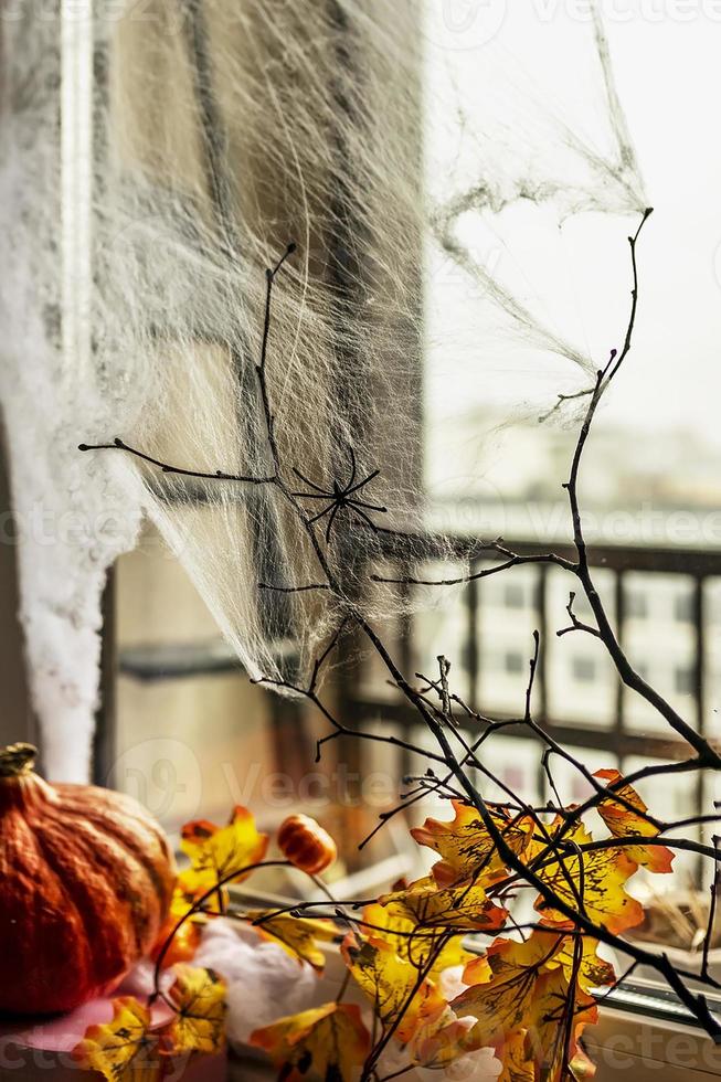 concepto de halloween, ventana decorada con telarañas, hojas amarillas de otoño, ramas de árboles desnudas y una calabaza en un fondo oscuro foto