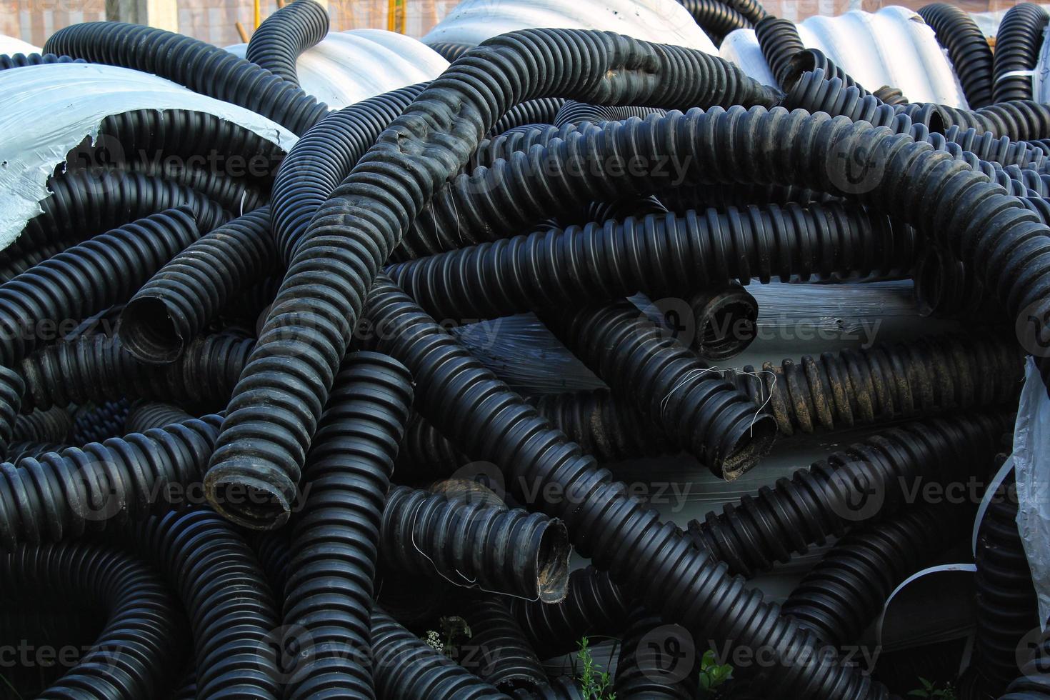 Rolled up pile of twisted, high pressure flexible black rubber pvc plastic hoses, construction material and equipment at building site. Conduit, goffred tubing pipes. Drain sewage tube pipeline photo