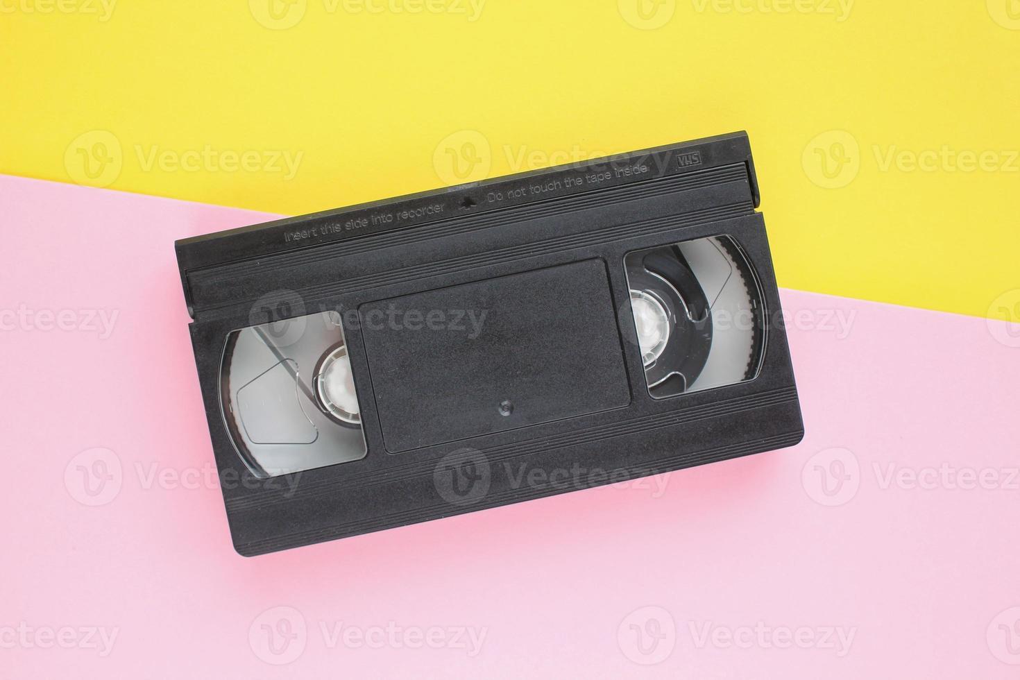 Black VHS videotape cassette on yellow and pink background. Old obsolete technology for tape recording and watching media movies. Retro, vintage, history, nostalgia concept. Top view, flat lay photo