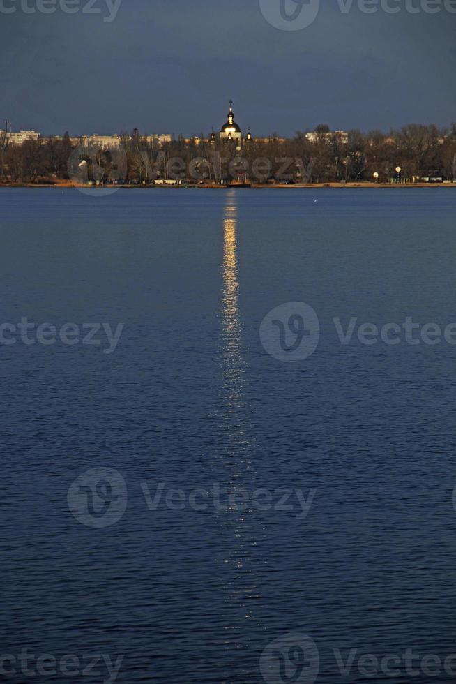 la cúpula dorada de la iglesia ortodoxa, de pie a orillas del río, se refleja en la superficie del agua. pasarela dorada desde la cúpula de la iglesia en la superficie del río. foto