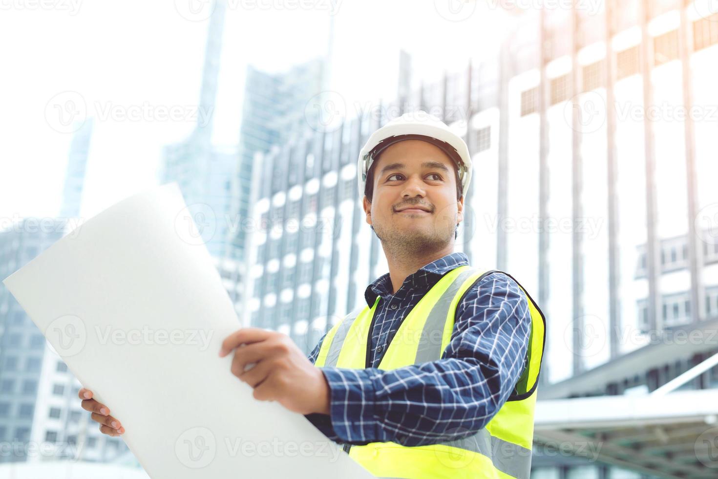 retrato de un trabajador de la construcción asiático de ingeniería que sostiene un rollo de papel de dibujo del casco blanco de seguridad del plan estructural y usa ropa reflectante para la seguridad de la operación de trabajo. foto