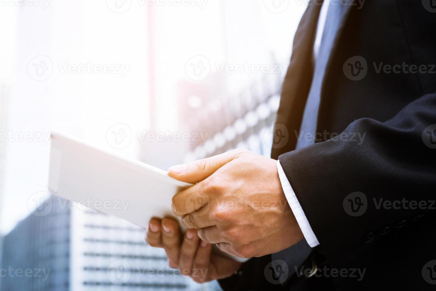 close up hand businessman working using a digital tablet pc device while standing in front of windows in an office building overlooking the city. photo