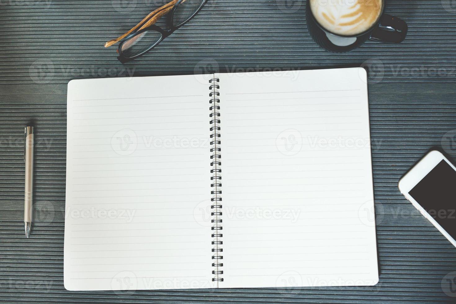 abra la mesa de escritorio de la oficina del bloc de notas de la página con el libro, el teléfono, los suministros del equipo en el trabajo y la taza de café. vista superior con espacio de copia en el papel de la página. foto