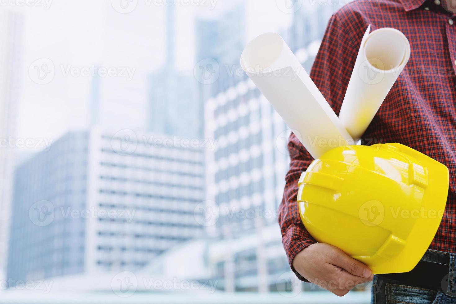 Close up of engineering male construction worker holding roll paper blueprint of drawing plan project and safety white helmet outdoor of building background. copy leave space for text. photo