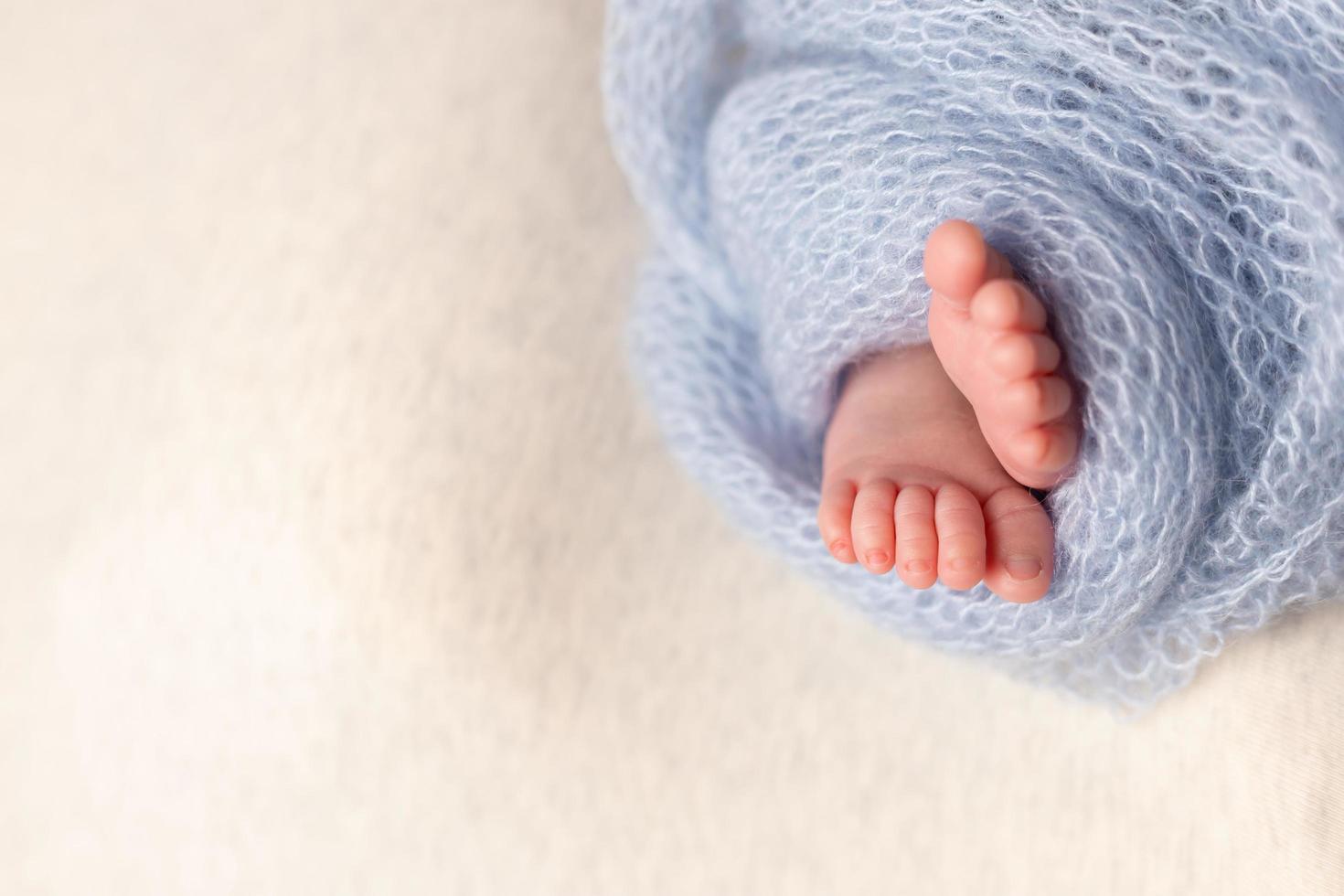 Newborn baby feet on an oatmeal background wrapped in a knitted blanket photo