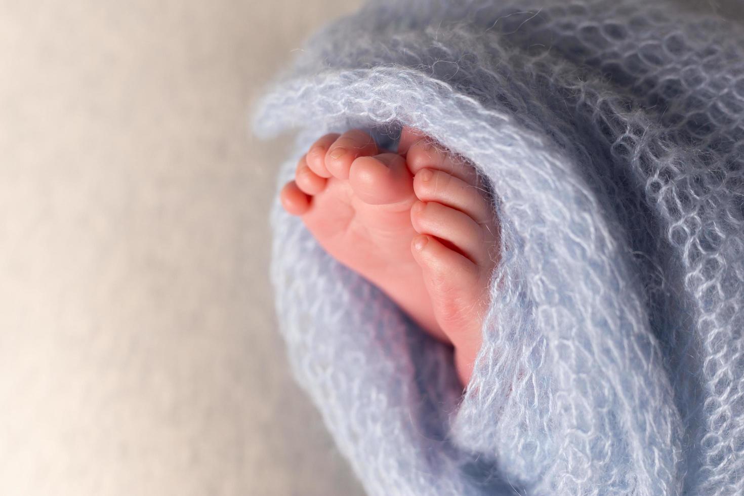 Newborn baby feet on an oatmeal background wrapped in a knitted blanket photo