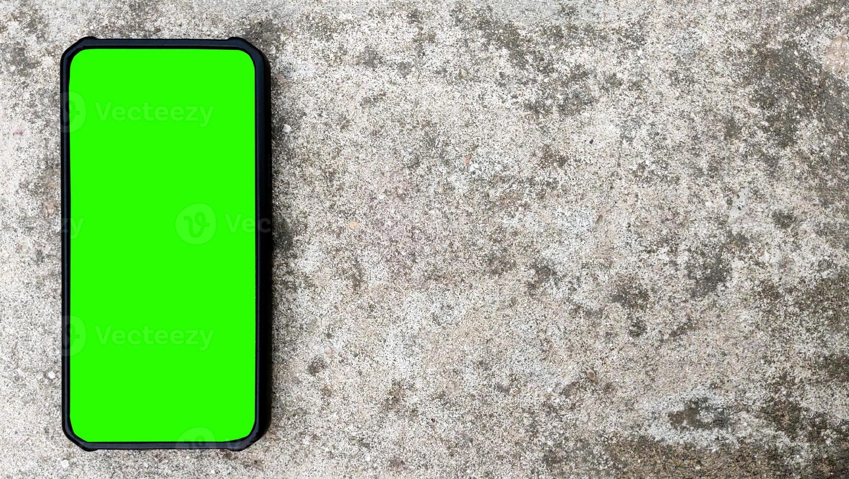 toma en ángulo superior de un smartphone negro con pantalla verde sobre fondo de hormigón. copiar espacio para texto foto