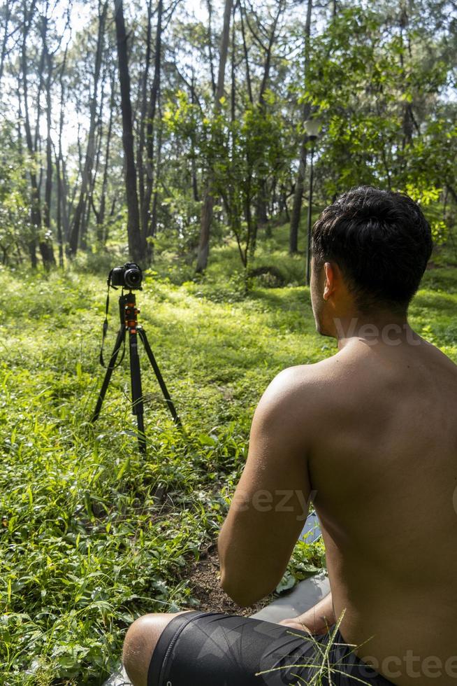 Millennial guy meditating with trainer online via tablet ipad connection, in the forest, broadcasting online your class and instructions, mexico photo