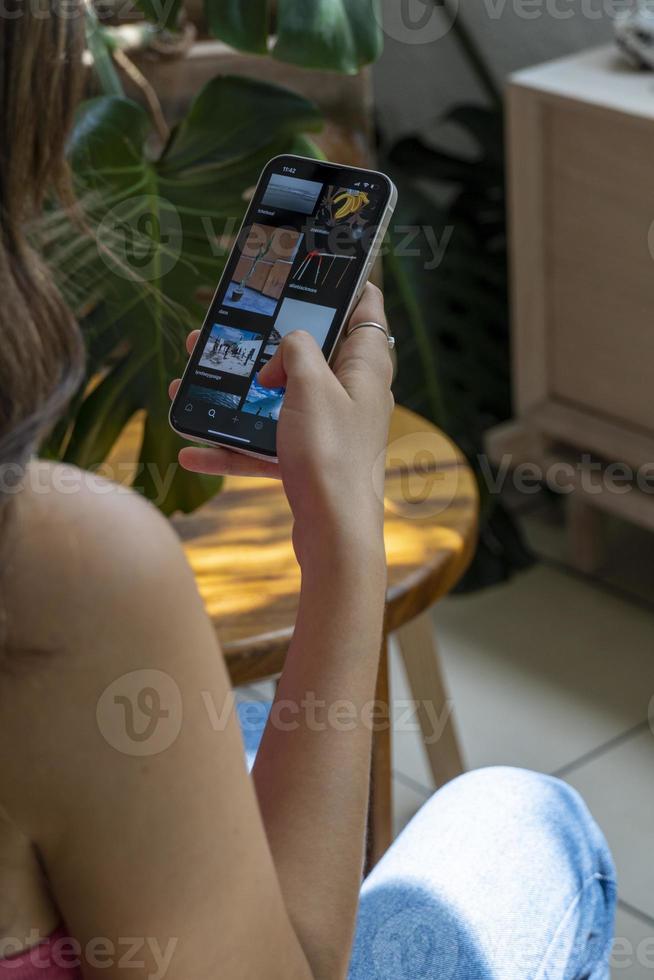 Happy millennial hispanic teen girl checking social media holding smartphone at home. photo