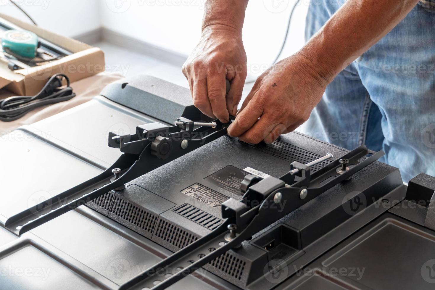 man installing the wall base for the television, it is a smart tv, adjusting with screwdriver photo
