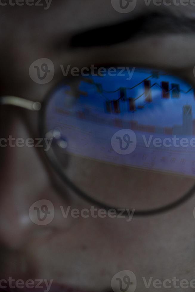 young woman, watching the stock market at night, the same market is seen in the reflection of her glasses photo