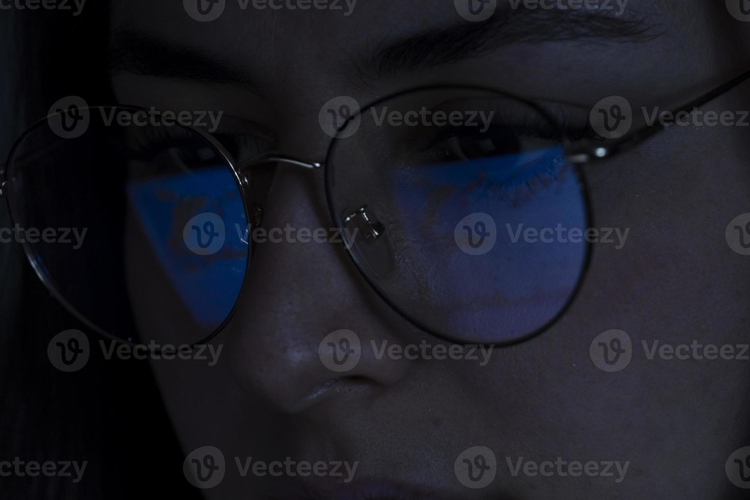 young woman, watching the stock market at night, the same market is seen in the reflection of her glasses photo