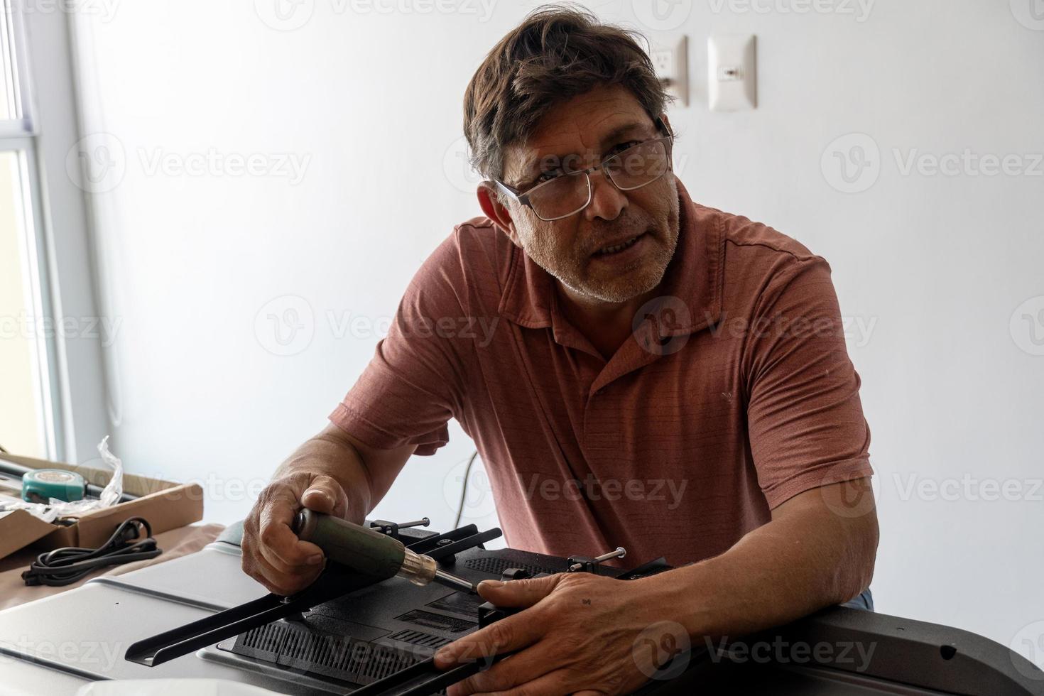 hombre latino poniendo una base para la televisión para que se pueda fijar a la pared foto