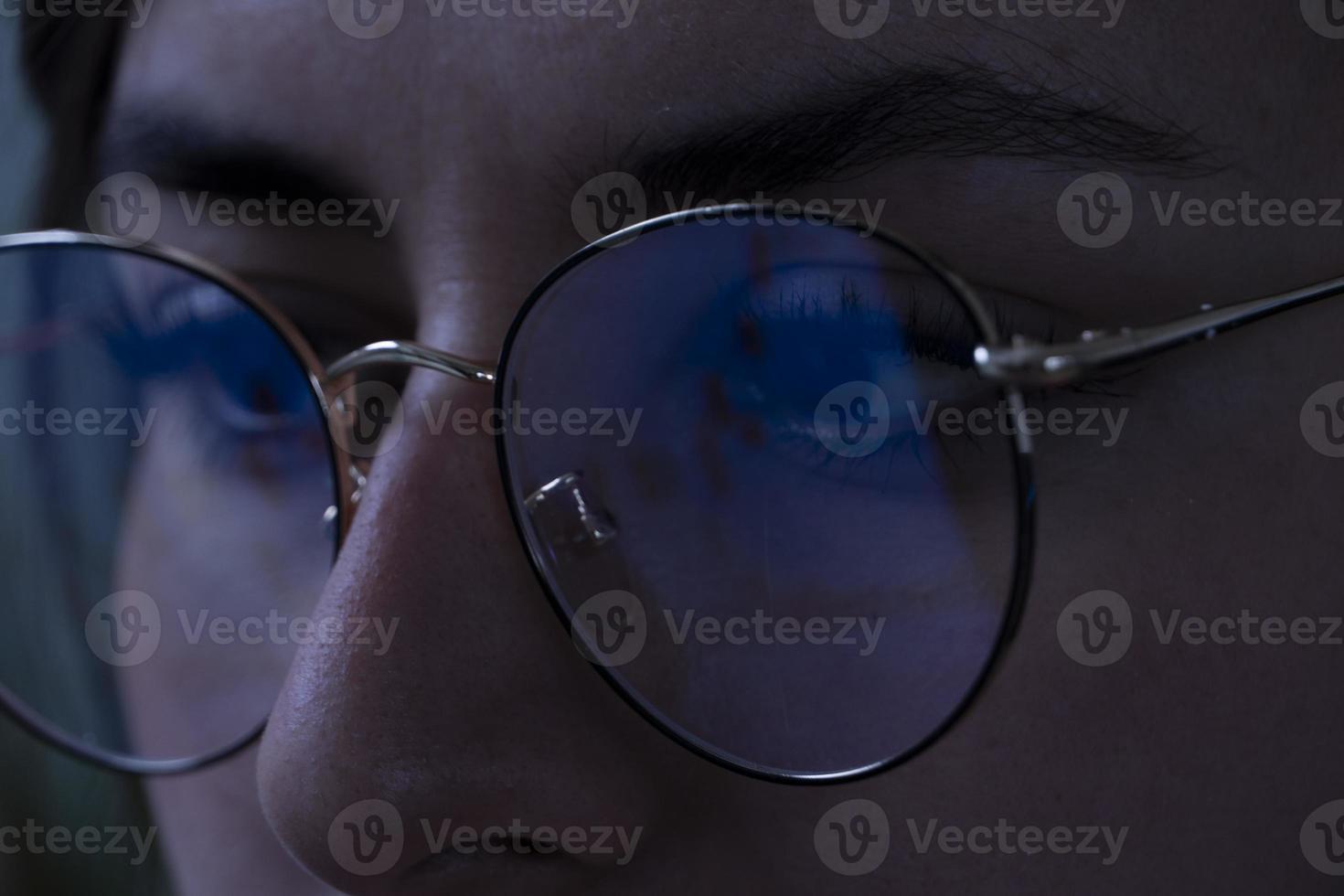 young woman, watching the stock market at night, the same market is seen in the reflection of her glasses photo