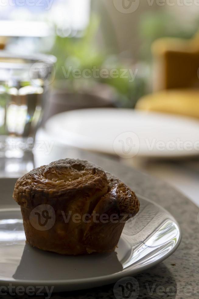 pancake or cupcake on ceramic plate, terrazzo table, in the background out of focus armchairs and glass of water photo