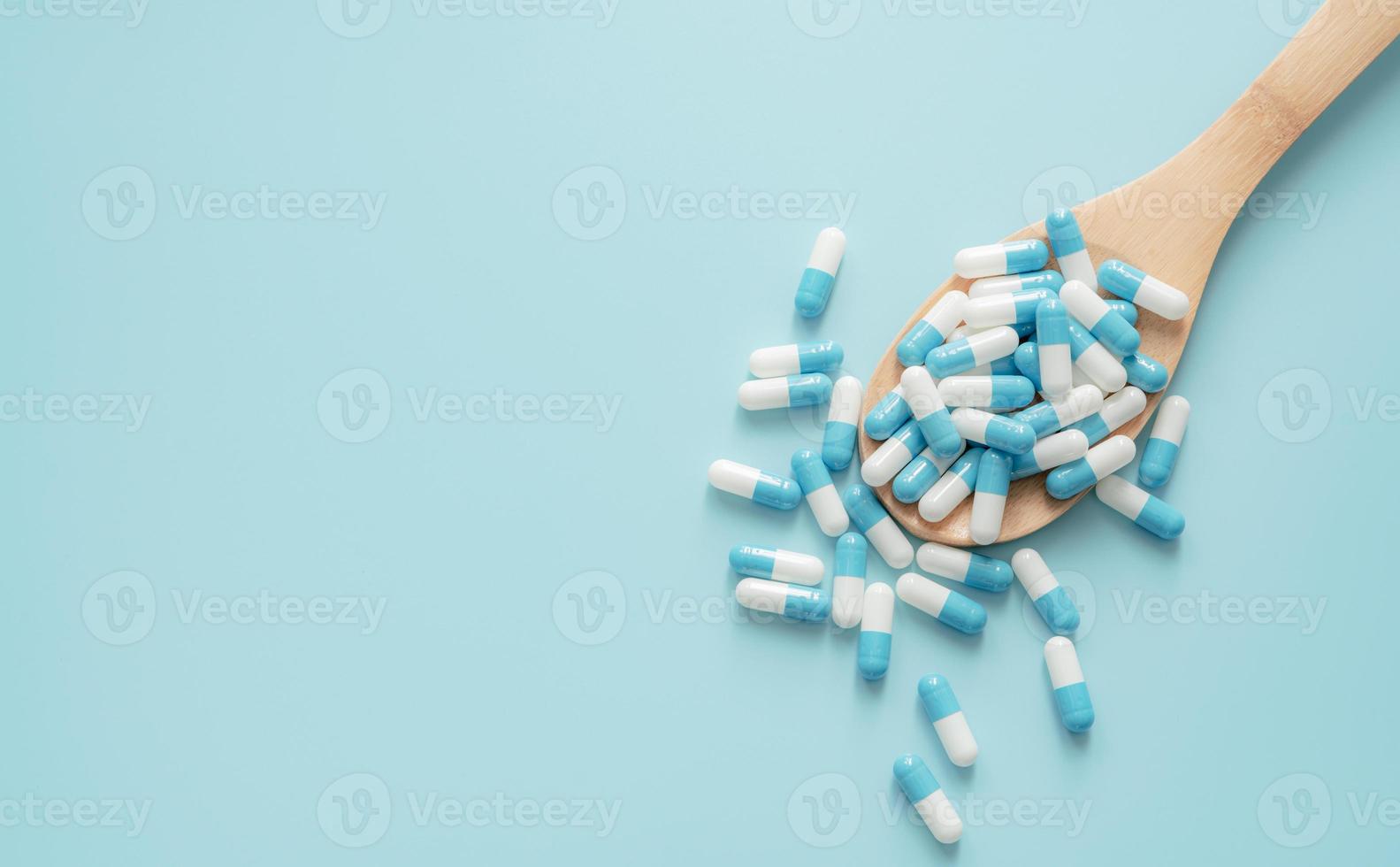 Top view of blue-white antibiotic capsule pills on wooden spoon and blue background. Antibiotic drug resistance. Prescription drug. Medical care. Pharmaceutical care. Antimicrobial drug overuse. photo