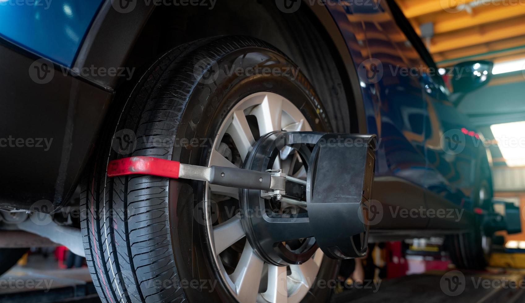 Wheel alignment equipment grip the tire of car wheel in car repair shop. Auto wheel alignment in workshop of service station. Car wheel balance. Suspension adjustment. Vehicle inside garage workshop. photo