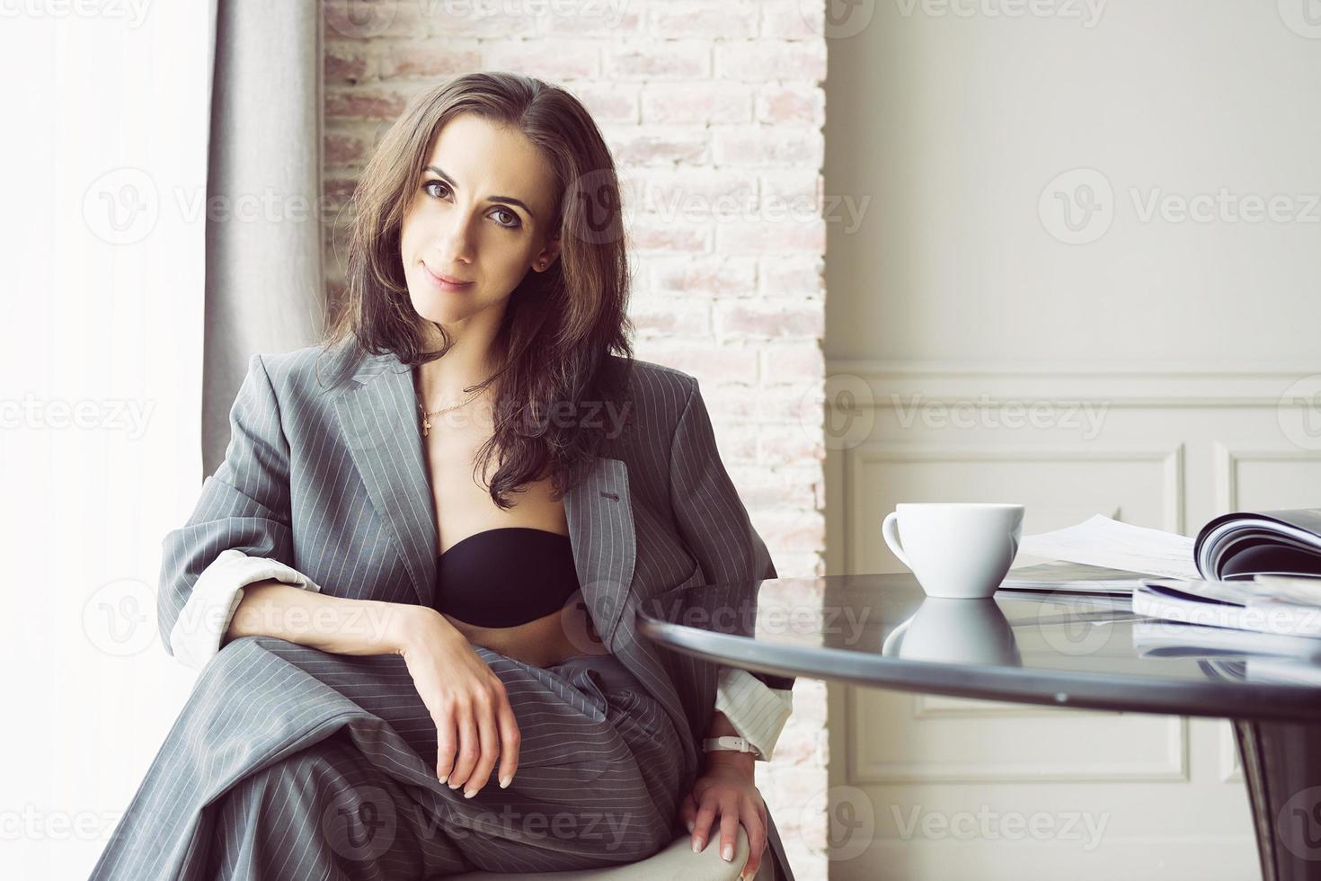 ballerina in a gray striped suit with a cup of coffee smiling and dreaming is sitting at a table by the window photo