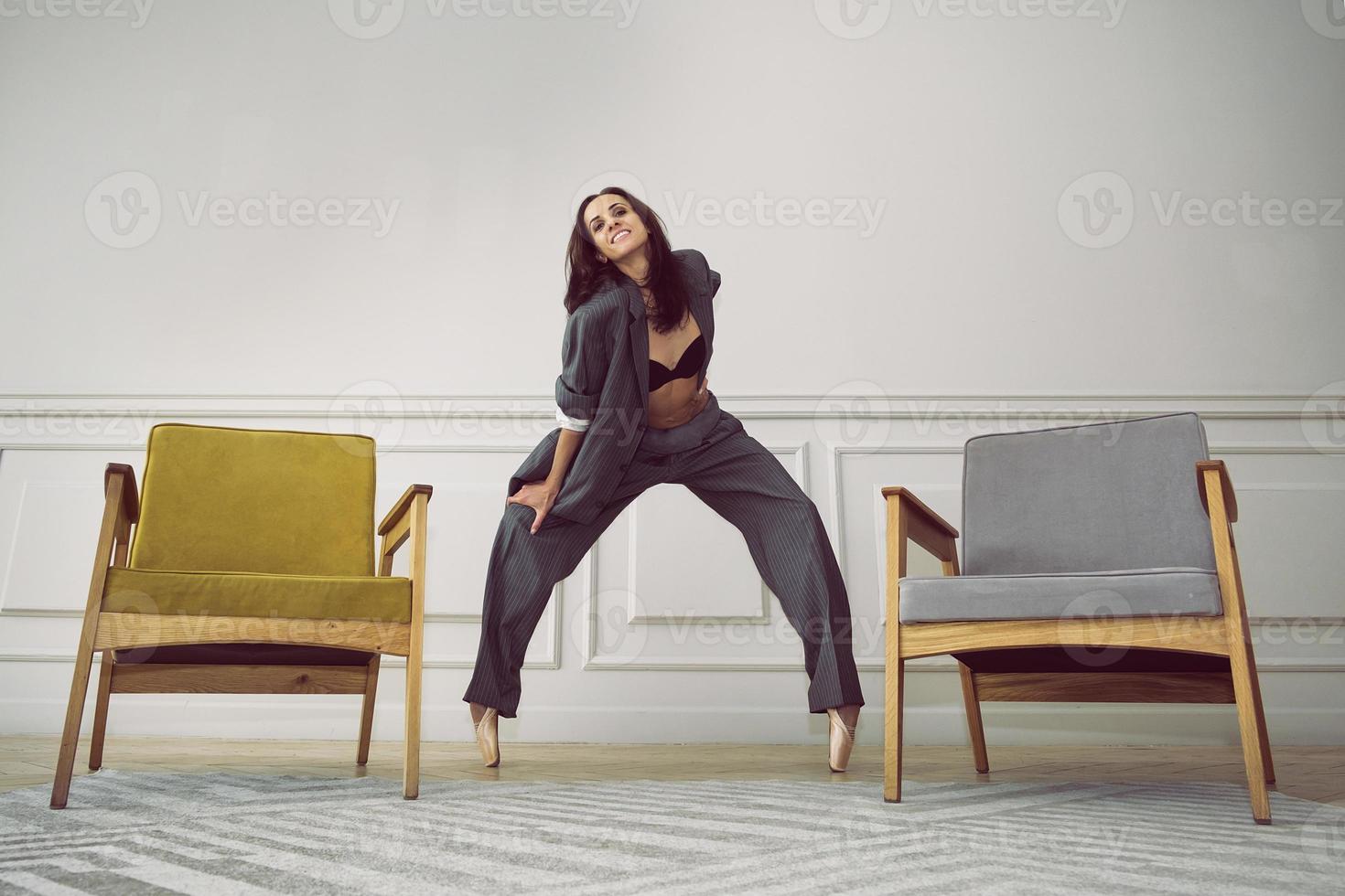 ballerina in a gray striped suit stands between the chairs on pointe shoes in a plie photo