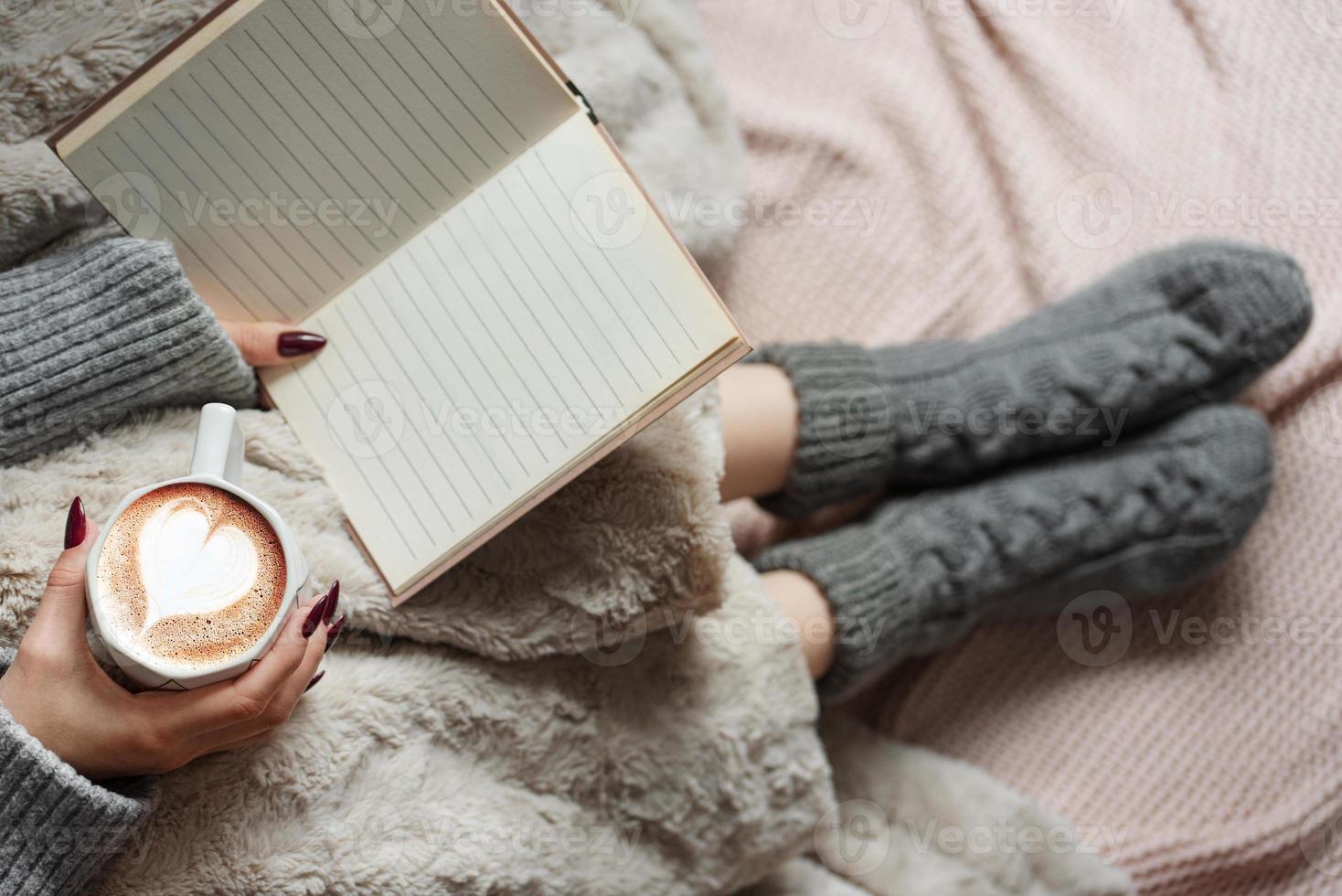 hogar acogedor, mujer cubierta con una manta cálida, bebe café y lee el libro. foto