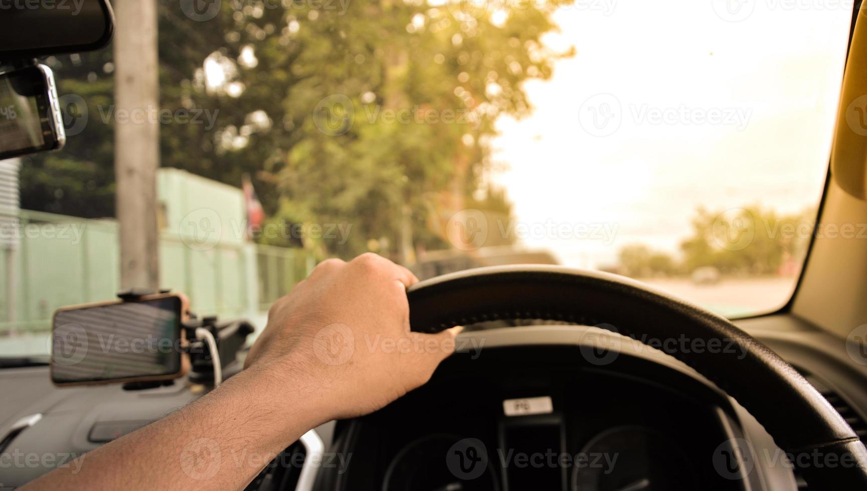 Man's hand holding steering wheel of a black car, blurry background, orange light photo