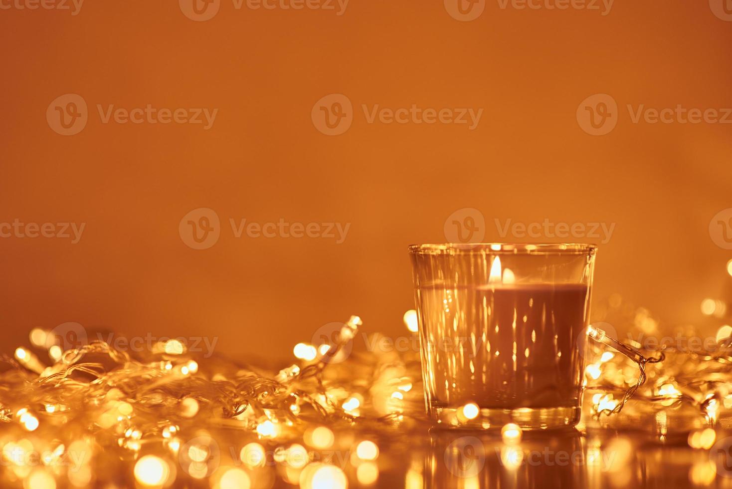 Burning candle with a golden garland lights in bokeh on dark background photo