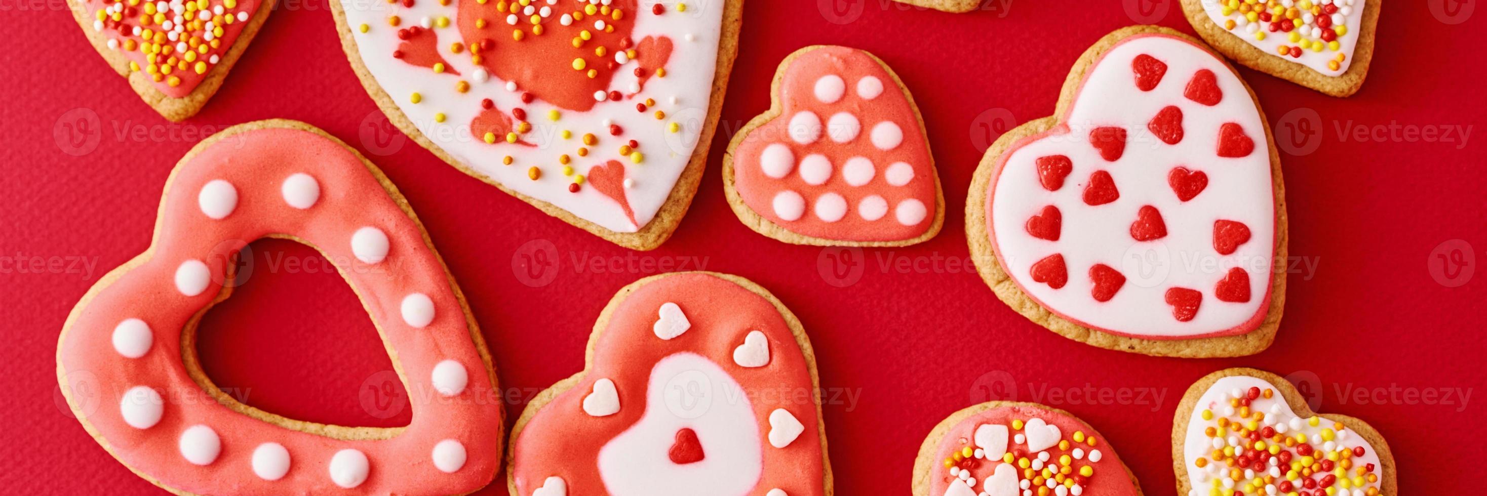 Background of decorated with icing and glazed heart shape cookies on the red background, long banner. Valentines Day food concept photo