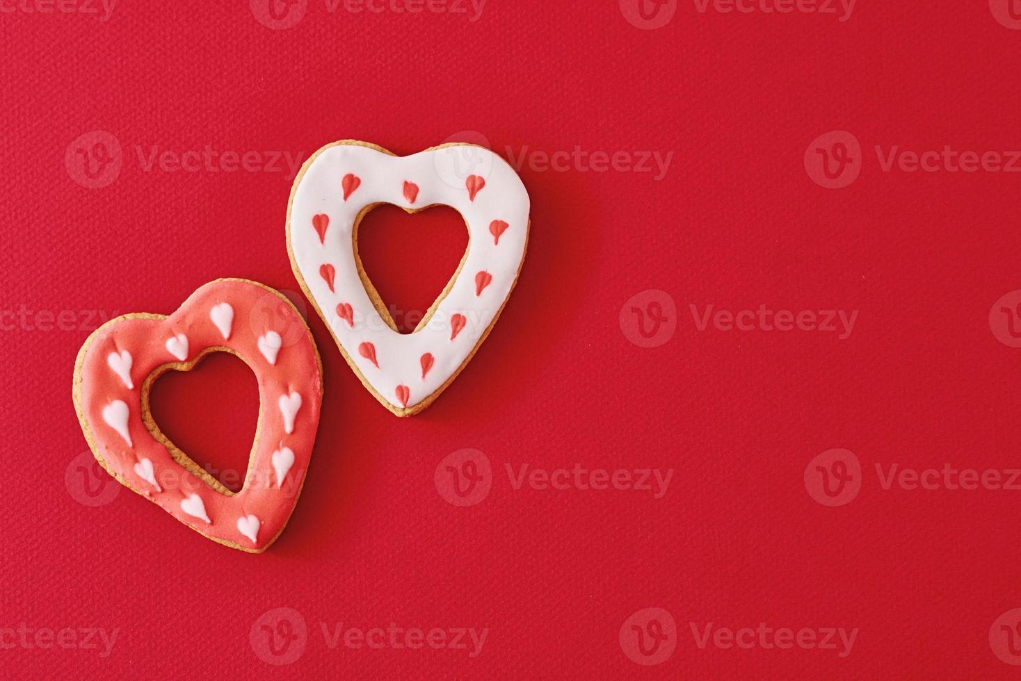 Two decorated with icing and glazed heart shape cookies on the red background with copy space. Valentines Day food concept photo